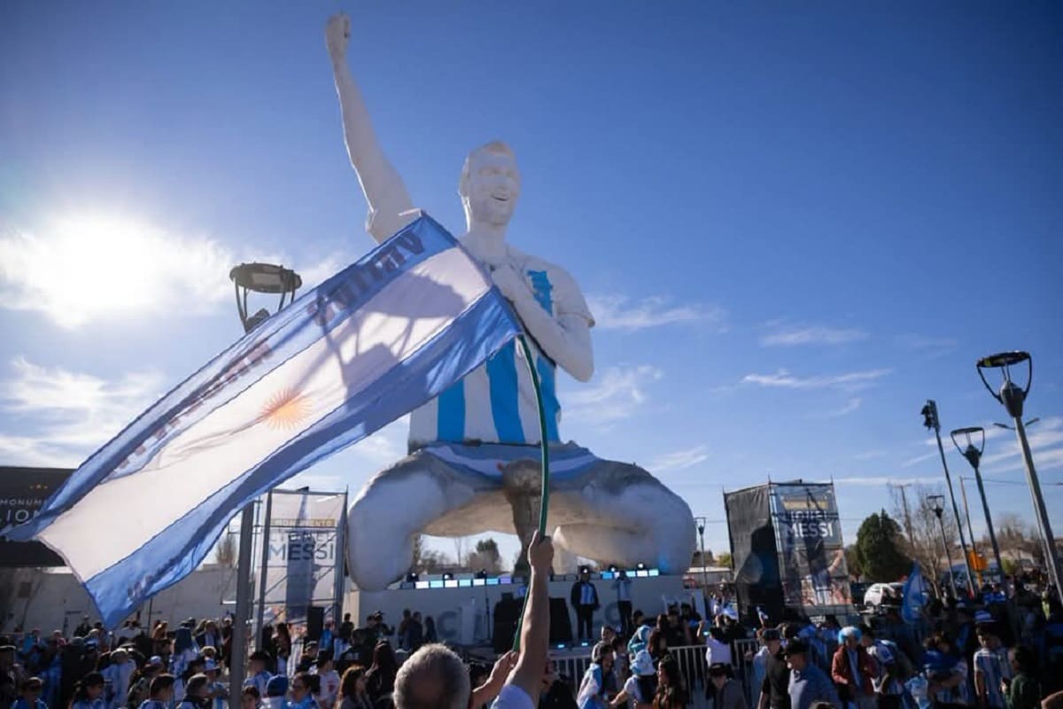 Estatua monumental de Lionel Messi en Neuquén, Argentina, con una multitud de seguidores y una bandera argentina