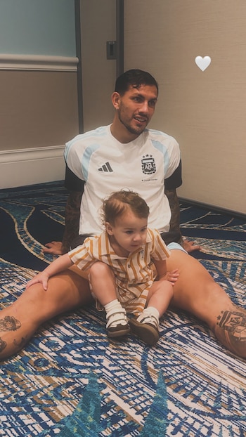 Jugador de la selección argentina sentado en el suelo con un niño pequeño en su regazo